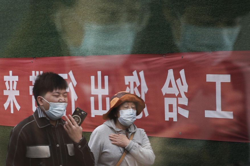 Commuters wearing face masks to help curb the spread of the coronavirus are reflected on a window panel as others walk by an office building under renovation in Beijing, Wednesday, Oct. 14, 2020. (AP Photo/Andy Wong)