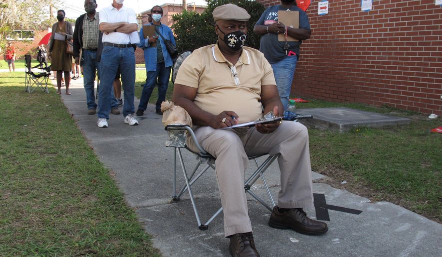 Richard Williams sits in a folding chair, filling out paperwork, as he waits in line to vote early in Savannah, Ga., on Wednesday, Oct. 14, 2020. Black people are going to the polls by the thousands and waiting in lines for hours to vote early in Georgia. (AP Photo/Russ Bynum)