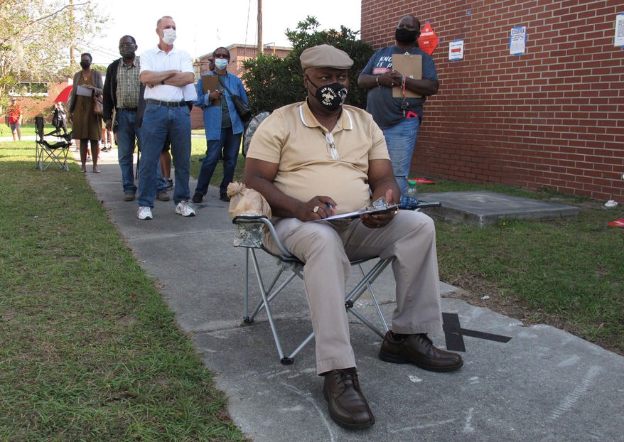 Richard Williams sits in a folding chair, filling out paperwork, as he waits in line to vote early in Savannah, Ga., on Wednesday, Oct. 14, 2020. Black people are going to the polls by the thousands and waiting in lines for hours to vote early in Georgia. (AP Photo/Russ Bynum)