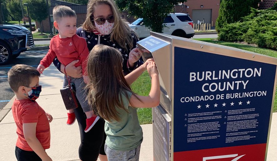 Nicole Flaherty, top, stands with her kids as her 7-year old daughter Madelyn places the ballot in the box in the Burlington County ballot box in Cinnaminson, N.J. on Wednesday, Oct. 7, 2020. While holding 1-year-old Colin, she opens the dropbox door as 5-year-old James, left, watches Madelyn push the ballots through the slot. (AP Photo/Christina Paciolla)