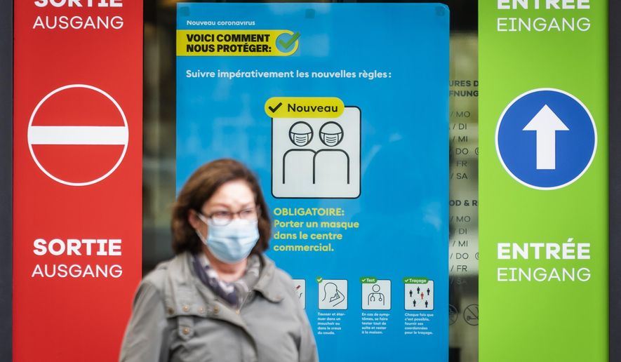A woman wearing a protective mask walks in front of a FOPH poster in front of a shopping centre in Fribourg, Switzerland, Friday, Oct. 16, 2020. Europe is at a “turning point” in the fight against the coronavirus, said Bertrand Levrat, head of Switzerland’s biggest hospital complex, acknowledging growing public fatigue over anti-COVID measures but says people must buckle down as Switzerland grapples with record daily case counts with measures like limiting the size of gatherings and stripping soldiers of weekend leave.(Jean-Christophe Bott/Keystone via AP)
