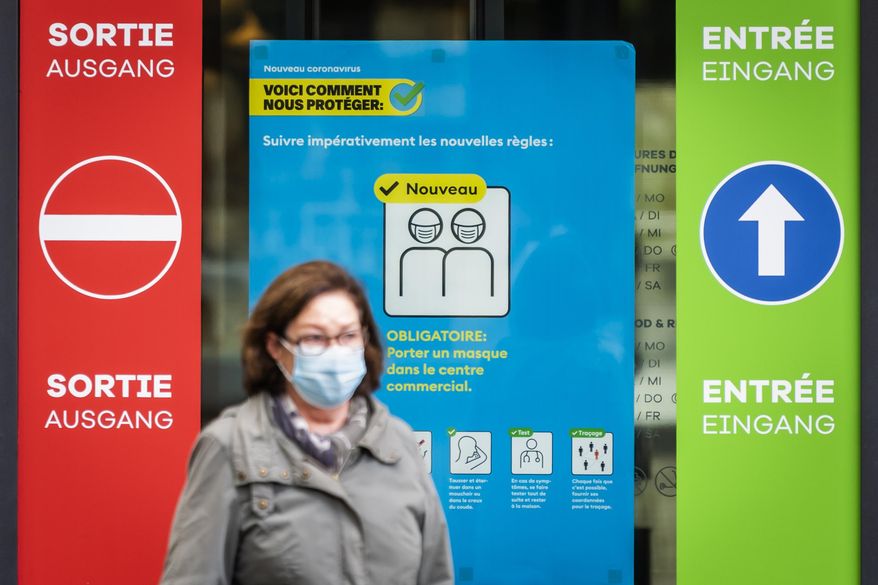 A woman wearing a protective mask walks in front of a FOPH poster in front of a shopping centre in Fribourg, Switzerland, Friday, Oct. 16, 2020. Europe is at a “turning point” in the fight against the coronavirus, said Bertrand Levrat, head of Switzerland’s biggest hospital complex, acknowledging growing public fatigue over anti-COVID measures but says people must buckle down as Switzerland grapples with record daily case counts with measures like limiting the size of gatherings and stripping soldiers of weekend leave.(Jean-Christophe Bott/Keystone via AP)