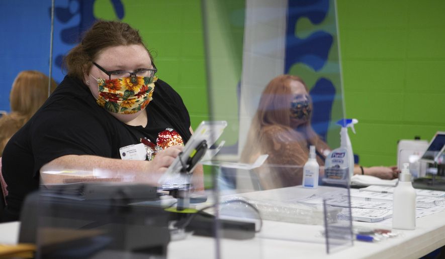 FILE - In this Aug. 4, 2020 file photo, Emily Salsbury, left, wipes off her tablet while she works the registration table for primary elections in Topeka, Kan. Kansas counties are making their own rules about whether to require poll workers to wear masks as the public votes. Secretary of State Scott Schwab has not issued a mandate requiring masks for poll workers statewide, even though the state spent $1.28 million to buy personal protective equipment for every polling location. (Evert Nelson/The Topeka Capital-Journal via AP, File)