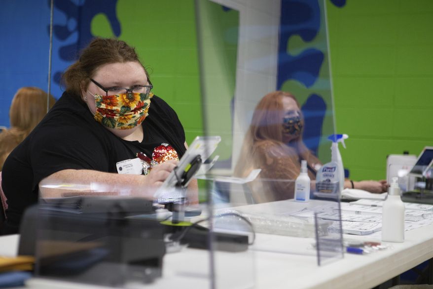 FILE - In this Aug. 4, 2020 file photo, Emily Salsbury, left, wipes off her tablet while she works the registration table for primary elections in Topeka, Kan. Kansas counties are making their own rules about whether to require poll workers to wear masks as the public votes. Secretary of State Scott Schwab has not issued a mandate requiring masks for poll workers statewide, even though the state spent $1.28 million to buy personal protective equipment for every polling location. (Evert Nelson/The Topeka Capital-Journal via AP, File)