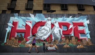 Women walk past a graffiti &amp;quot;Hope&amp;quot; painted on metals barrier that closed the entrance of a hotel that was damaged by Aug. 4 explosion that hit the seaport of Beirut, Lebanon, Monday, Oct. 12, 2020. A year ago, hundreds of thousands of Lebanese took to the streets in protests nationwide that raised hopes among many for a change in a political elite that over that decades has run the country into the ground.  (AP Photo/Bilal Hussein)