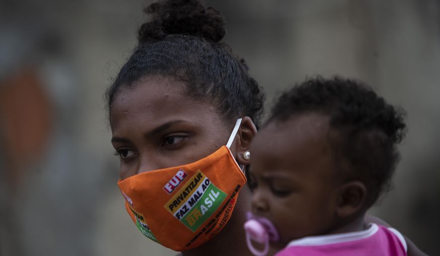 Carolaine Rocha, 22, holds her son while waiting to receive donated food from Petrobras workers and the oil workers union via the Tankers’ Campaign that provide a supplement for the poor caught by declining wages and jobs due to the new coronavirus pandemic, in the Vila Vintem neighborhood of Rio de Janeiro, Brazil, Friday, Oct. 16, 2020. Rocha says that the family&#39;s income comes from the money her husband makes as a barber. “The poor have to work, otherwise we don&#39;t eat. We can&#39;t expect anything from the government,” she said. (AP Photo/Bruna Prado)