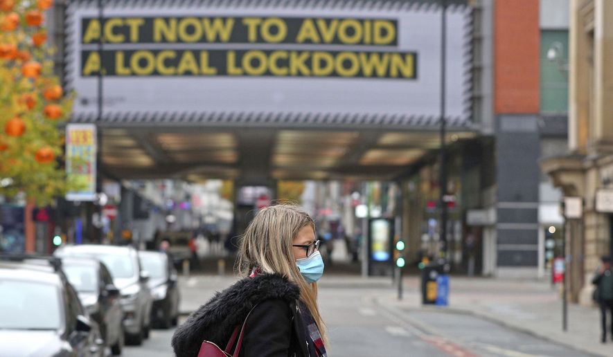 A woman wearing a face mask walks in Manchester, England, Monday, Oct. 19, 2020. Britain’s government says discussions about implementing stricter restrictions in Greater Manchester must be completed Monday because the public health threat caused by rising COVID-19 infections is serious and getting worse. (Peter Byrne/PA via AP)