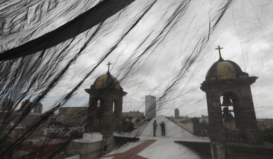 Men are seen through safety netting as they stand atop a less-damaged section of Nuestra Senora de Los Angeles, or Our Lady of Angels church, during the early stages of reconstruction work, three years after an earthquake collapsed nearly half of the church's 18th-century dome in Mexico City, Friday, Oct. 16, 2020. The experts working on projects like this across Mexico face some of the same issues confronting restorers everywhere, like France’s re-building of the Notre Dame Cathedral: are the materials and craftsmen's skills of centuries ago still available? (AP Photo/Rebecca Blackwell)