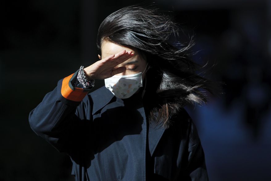 A woman wearing a face mask to help curb the spread of the coronavirus uses her hand to shield from the wind on a street in Beijing, Wednesday, Oct. 21, 2020. (AP Photo/Andy Wong)