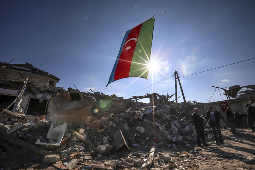 Azerbaijan&#39;s national flag flies over destroyed houses in a residential area that was hit by rocket fire overnight by Armenian forces, on Thursday, Oct. 22, 2020 in Ganja, Azerbaijan&#39;s second largest city, near the border with Armenia. Heavy fighting over Nagorno-Karabakh is continuing with Armenia and Azerbaijan trading blame for new attacks. The nearly four weeks of hostilities have raised the threat of Turkey and Russia being drawn into the conflict. (AP Photo/Aziz Karimov)