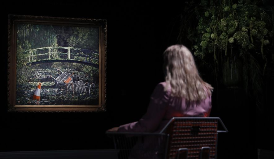 A member of staff poses in front of a work of art by Banksy entitled 'Show Me The Monet" at Sotheby's auction house in London, Friday, Oct. 16, 2020. The painting is valued at 3-5 million pounds (US$ 3.8-6.4 million ) when sold at auction on Oct. 21. (AP Photo/Alastair Grant)
