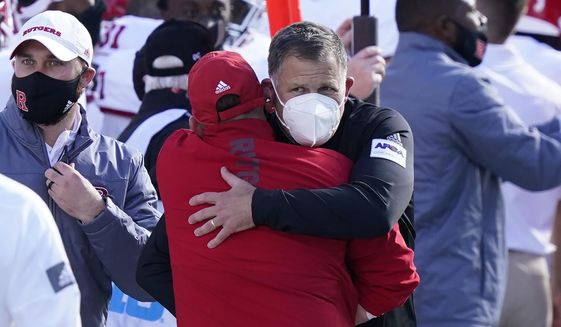 Rutgers head coach Greg Schiano, with a mask, is hugged by an assistant after his team defeated Michigan State in an NCAA college football game, Saturday, Oct. 24, 2020, in East Lansing, Mich. (AP Photo/Carlos Osorio)