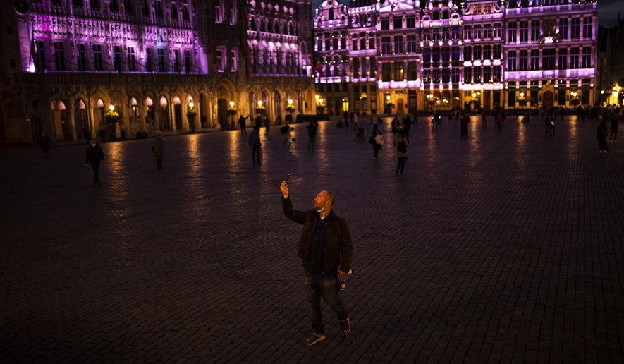 A passersby strolls and takes photographs on Grand Place during an autumn evening prior to the curfew in downtown Brussels, Friday, Oct. 23, 2020. In much of Europe, city squares and streets, be they wide, elegant boulevards like in Paris or cobblestoned alleys in Rome, serve as animated evening extensions of drawing rooms and living rooms. As Coronavirus restrictions once again put limitations on how we live and socialize, AP photographers across Europe delivered a snapshot of how Friday evening, the gateway to the weekend, looks and feels. (AP Photo/Francisco Seco)