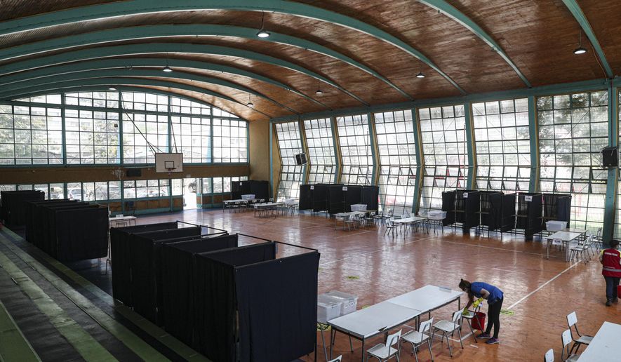 A worker wipes a chair during a disinfection operation amid the COVID-19 pandemic, at a gymnasium that will serve as a polling station for a constitutional plebiscite, in Santiago, Chile, Saturday, Oct. 24, 2020. Chileans will decide on Sunday whether or not to replace the constitution that dates back to the dictatorship of Augusto Pinochet, and secondly, if the current Congress or other citizens should write the new text. (AP Photo/Esteban Felix)