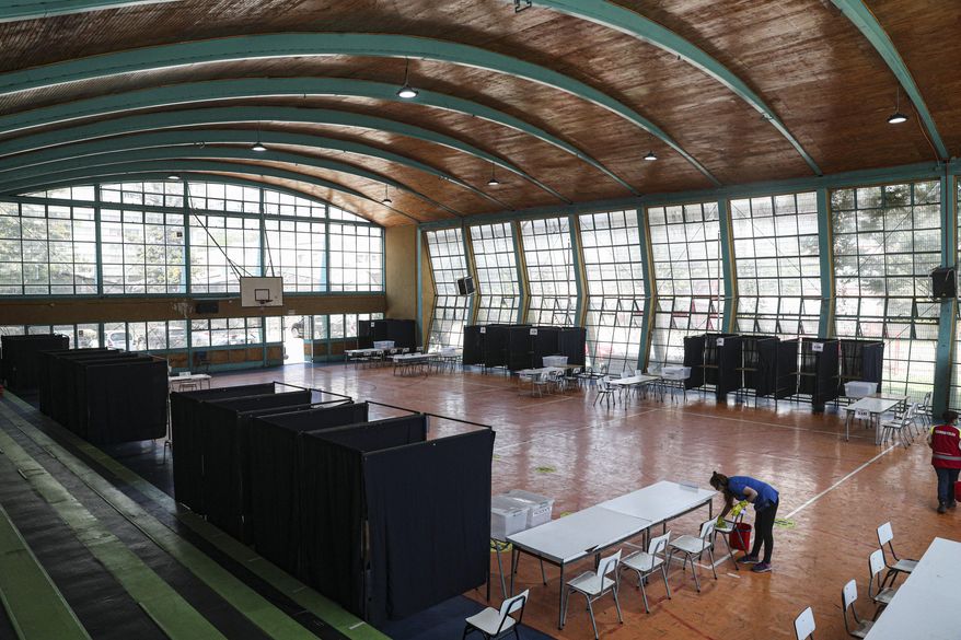 A worker wipes a chair during a disinfection operation amid the COVID-19 pandemic, at a gymnasium that will serve as a polling station for a constitutional plebiscite, in Santiago, Chile, Saturday, Oct. 24, 2020. Chileans will decide on Sunday whether or not to replace the constitution that dates back to the dictatorship of Augusto Pinochet, and secondly, if the current Congress or other citizens should write the new text. (AP Photo/Esteban Felix)
