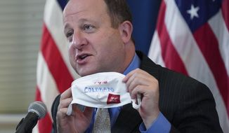 FILE - In this Tuesday, Oct. 20, 2020, file photo, Colorado Gov. Jared Polis holds up a face mask featuring the state&#39;s new advertising campaign to encourage residents to protect against COVID-19 during a news conference about the steady increase in cases of the new coronavirus in the state in Denver. Colorado Gov. Polis is quarantining himself after learning that Aurora Mayor Mike Coffman tested positive for the coronavirus. Coffman&#39;s diagnosis on Sunday, Oct. 25, 2020, came over a week after he and the governor appeared with other officials at a news conference. A Polis spokesperson said the governor would quarantine while waiting to hear from contact tracers. Coffman said he worked from home starting Thursday after not feeling well and his symptoms were gone by Saturday. He says he got a rapid test Sunday in hopes of being cleared to return to his office and schedule but will now quarantine at home. (AP Photo/David Zalubowski, File)