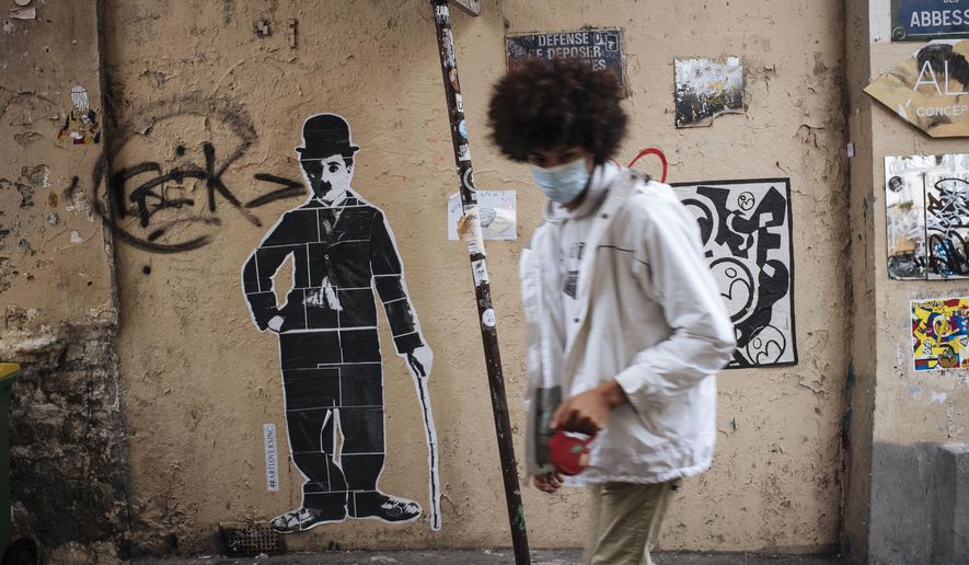 A man wearing a face mask, walks by a Charlie Chaplin street art, in the Montmartre district of Paris, Sunday Oct.25, 2020. A curfew intended to curb the spiraling spread of the coronavirus, has been imposed in many regions of France including Paris and its suburbs. (AP Photo/Lewis Joly)