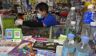 A newsstand vendor, wearing a mask to protect against the coronavirus, sits near QR codes for Alipay and WeChat, two popular online payment systems in Beijing, China on Tuesday, July 21, 2020. Ant Group, the financial technology arm of e-commerce giant Alibaba Group, on Tuesday, Aug. 25, 2020, filed for a dual-listing in Hong Kong and Shanghai, in what would likely be the world’s largest initial public stock offering since the coronavirus pandemic began. (AP Photo/Ng Han Guan, File)