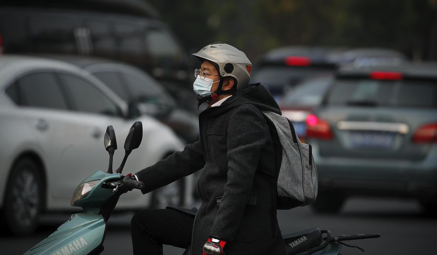 A man wearing a face mask to help curb the spread of the coronavirus rides on a scooter as he waits to cross a street during the morning rush hour in Beijing, Monday, Oct. 26, 2020. Schools and kindergartens have been suspended and communities are on lockdown in Kashgar, a city in China&#39;s northwest Xinjiang region, after more than 130 asymptomatic cases of the coronavirus were discovered. (AP Photo/Andy Wong)