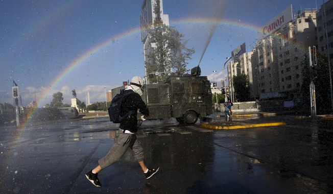 An anti-government protester runs from police water cannons, on the day Chileans vote in a referendum to decide whether the country should replace its 40-year-old constitution, written during the dictatorship of Gen. Augusto Pinochet, in Santiago, Chile, Sunday, Oct. 25, 2020. (AP Photo/Luis Hidalgo)