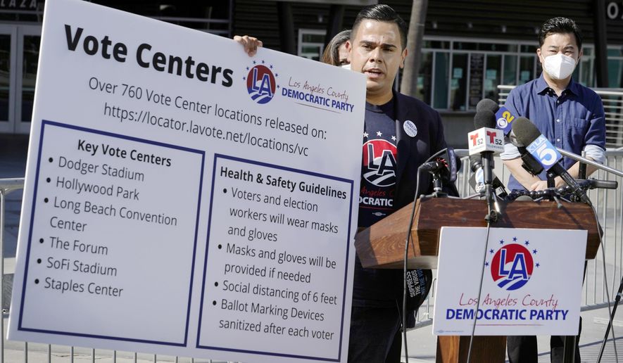 FILE - In this Oct. 1, 2020 file photo, Los Angeles County Democratic Party Chair Mark J. Gonzalez, center, flanked by Los Angeles City Councilmember David Ryu, right, and others, holds a banner with key vote center locations and social distancing instructions at a news conference outside Staples Center in Los Angeles. Most vote centers in California will open on Saturday. There will be fewer of them available this year because of the coronavirus. While most people will vote by mail, some will still show up to vote in person. State officials are urging people to vote early to avoid lines. (AP Photo/Damian Dovarganes, File)