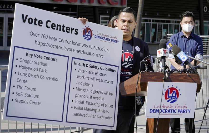 FILE - In this Oct. 1, 2020 file photo, Los Angeles County Democratic Party Chair Mark J. Gonzalez, center, flanked by Los Angeles City Councilmember David Ryu, right, and others, holds a banner with key vote center locations and social distancing instructions at a news conference outside Staples Center in Los Angeles. Most vote centers in California will open on Saturday. There will be fewer of them available this year because of the coronavirus. While most people will vote by mail, some will still show up to vote in person. State officials are urging people to vote early to avoid lines. (AP Photo/Damian Dovarganes, File)