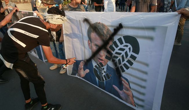Protesters deface a picture of French President Emmanuel Macron during a protest over caricatures of the Prophet Muhammad they deem insulting and blasphemous, outside the French Embassy, in Baghdad, Iraq, Monday, Oct. 26, 2020. Muslims in the Middle East and beyond on Monday called for boycotts of French products and for protests over the caricatures, but France&#x27;s president has vowed his country will not back down from its secular ideals and defense of free speech. (AP Photo/Khalid Mohammed)