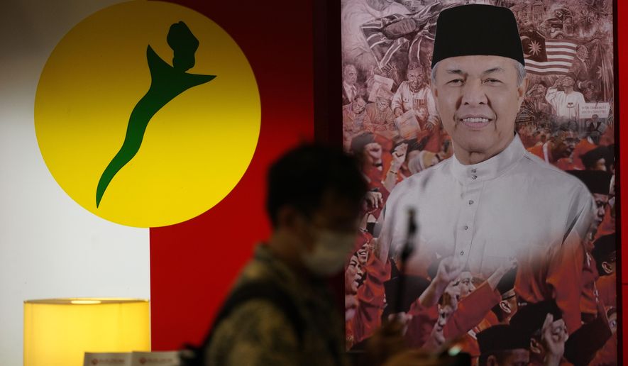 A man walks in front of a poster of UMNO ( United Malays National Organisation) President Ahmad Zahid at UMNO headquarter in Kuala Lumpur, Malaysia, Monday, Oct. 26, 2020. A key ally has reaffirmed support for Malaysian Prime Minister Muhyiddin Yassin&#x27;s government, offering him a respite after his failed bid to declare a coronavirus emergency,  but his political survival still hangs in the balance. The UMNO, the biggest party in the unelected governing coalition was angry at being sidelined amid rivalry with Muhyiddin&#x27;s own Malay party.   (AP Photo/Vincent Thian)