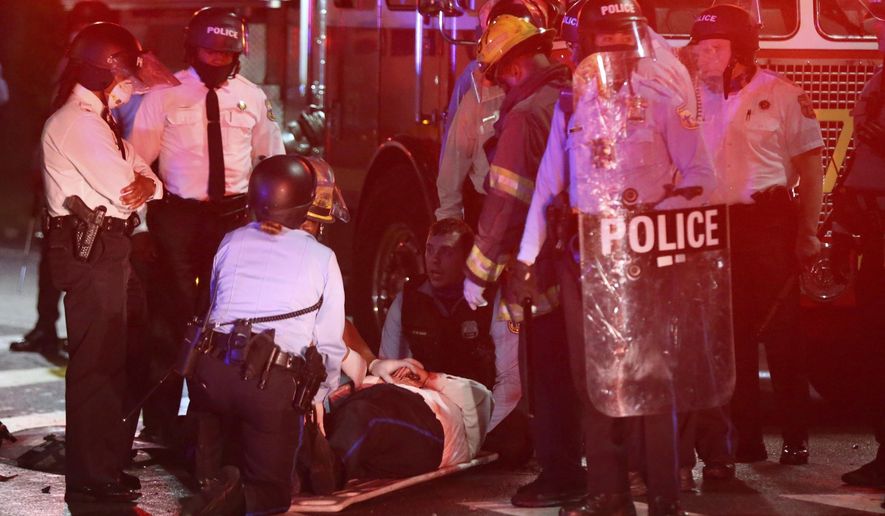 A police officer lies on the ground before being loaded into an ambulance on 52nd Street in West Philadelphia in the early hours of Tuesday, Oct. 27, 2020. Protesters gathered after police shot and killed a Black man in West Philadelphia on Monday. (Tim Tai/The Philadelphia Inquirer via AP)