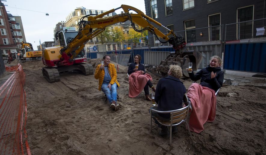 People enjoy a beer on an improvised beach terrace during road construction works outside a bar in Amsterdam, Netherlands, Friday, Oct. 23, 2020. Dutch bars and restaurants were closed as of last week as part of a "partial lockdown" announced by Prime Minister Mark Rutte. Shops and bars also have been banned from selling alcohol after 8 p.m. (AP Photo/Peter Dejong)