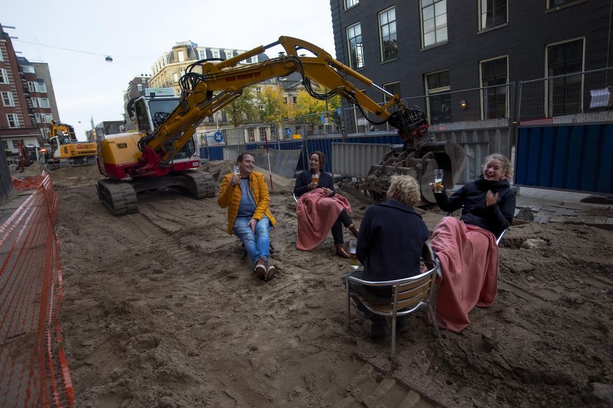 People enjoy a beer on an improvised beach terrace during road construction works outside a bar in Amsterdam, Netherlands, Friday, Oct. 23, 2020. Dutch bars and restaurants were closed as of last week as part of a "partial lockdown" announced by Prime Minister Mark Rutte. Shops and bars also have been banned from selling alcohol after 8 p.m. (AP Photo/Peter Dejong)