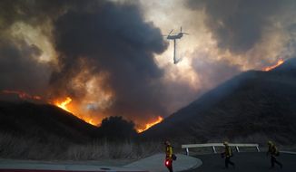 A helicopter drops water as firefighters walk with drip torches to set a backfire against the Blue Ridge Fire on Tuesday, Oct. 27, 2020, in Chino Hills, Calif. Facing extreme wildfire conditions this week that included hurricane-level winds, the main utility in Northern California cut power to nearly 1 million people while its counterpart in Southern California pulled the plug on just 30 customers to prevent power lines and other electrical equipment from sparking a blaze. (AP Photo/Jae C. Hong)