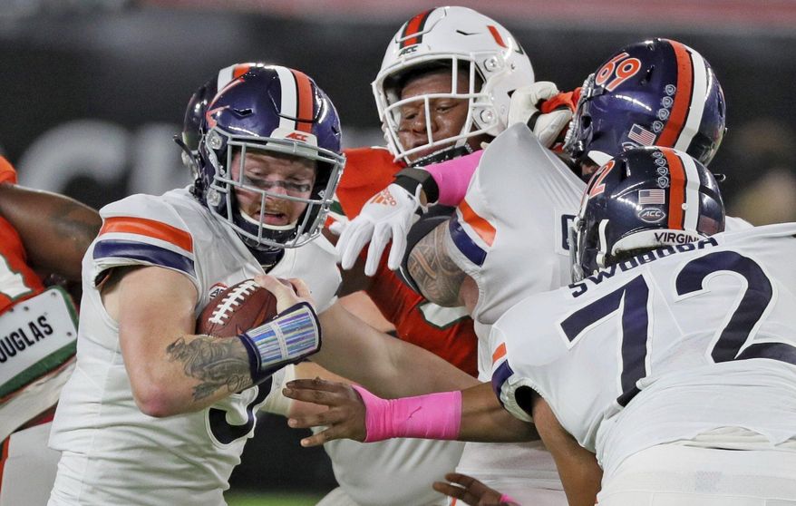 The Miami defense pressures Virginia quarterback Brennan Armstrong (5) on a keeper in the first quarter of an NCAA college football game in Miami Gardens, Fla., Saturday, Oct. 24, 2020. (Al Diaz/Miami Herald via AP)