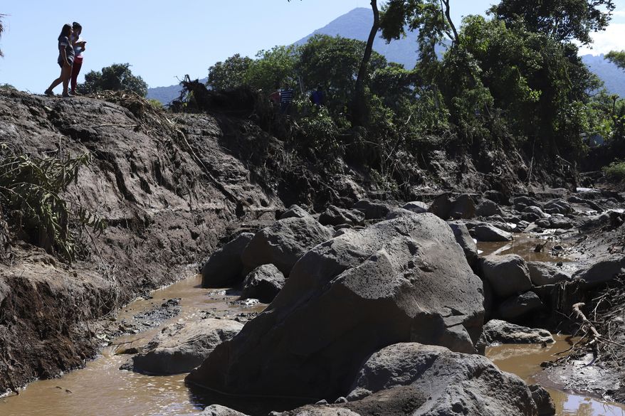 Women take pictures of an area destroyed by a deadly landslide in Nejapa, El Salvador, Friday, Oct. 30, 2020. The slide occurred Thursday night when earth from the upper part of the San Salvador volcano was set in motion, sweeping up trees and homes. (AP Photo/Salvador Melendez)