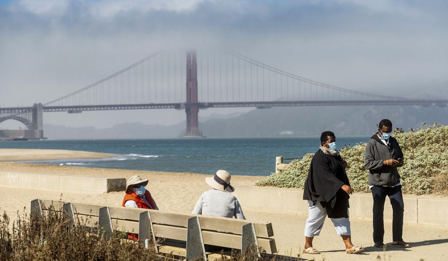 FILE - In this Oct. 22, 2020, file photo, with the Golden Gate Bridge in the background, people wear face masks while strolling at Crissy Field East Beach in San Francisco. San Francisco will temporarily halt the reopening of additional activities and businesses planned for next week week because of an increase in coronavirus case rates and hospitalizations, the city's mayor and health director said Friday, Oct. 30, 2020. (AP Photo/Noah Berger, File)