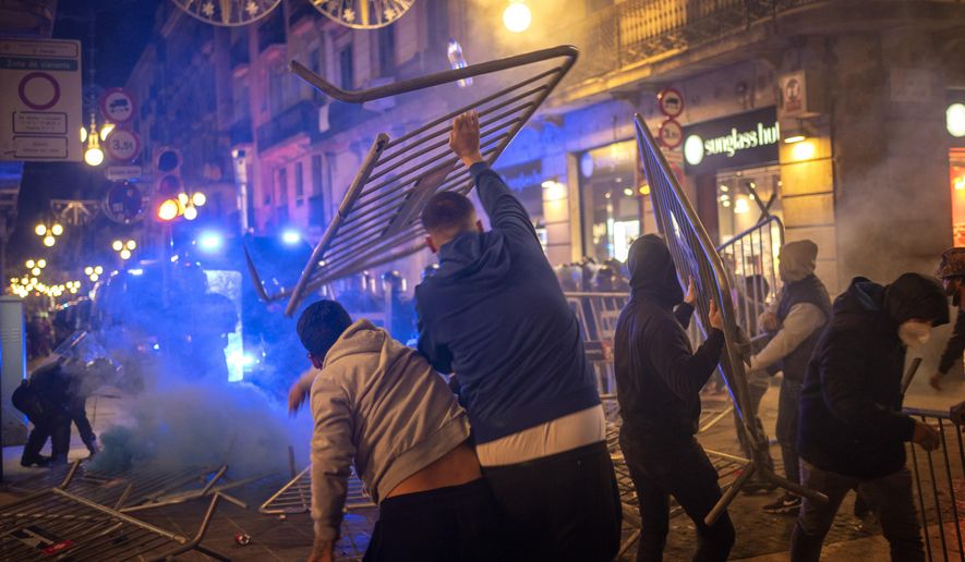 Demonstrators throw metallic fences against police during clashes in downtown Barcelona, Spain, Friday, Oct. 30, 2020. Clashes have erupted in a central Barcelona square between anti-riot police and hundreds who had gathered to protest the mandatory closure of bars, restaurants and other businesses in the latest effort to rein in on coronavirus outbreaks. (AP Photo/Emilio Morenatti)