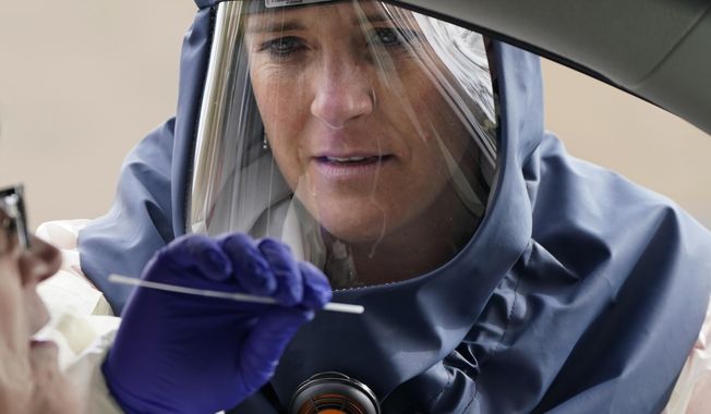 FILE - In this Friday, Oct. 23, 2020 file photo, Salt Lake County Health Department public health nurse Lee Cherie Booth performs a coronavirus test outside the Salt Lake County Health Department in Salt Lake City. Utah Gov. Gary Herbert and health officials issued repeated pleas for social distancing and mask usage on Thursday, Oct. 29, 2020, as hospitals grow closer to implementing crisis care protocols amid a record-breaking coronavirus surge. (AP Photo/Rick Bowmer, File)