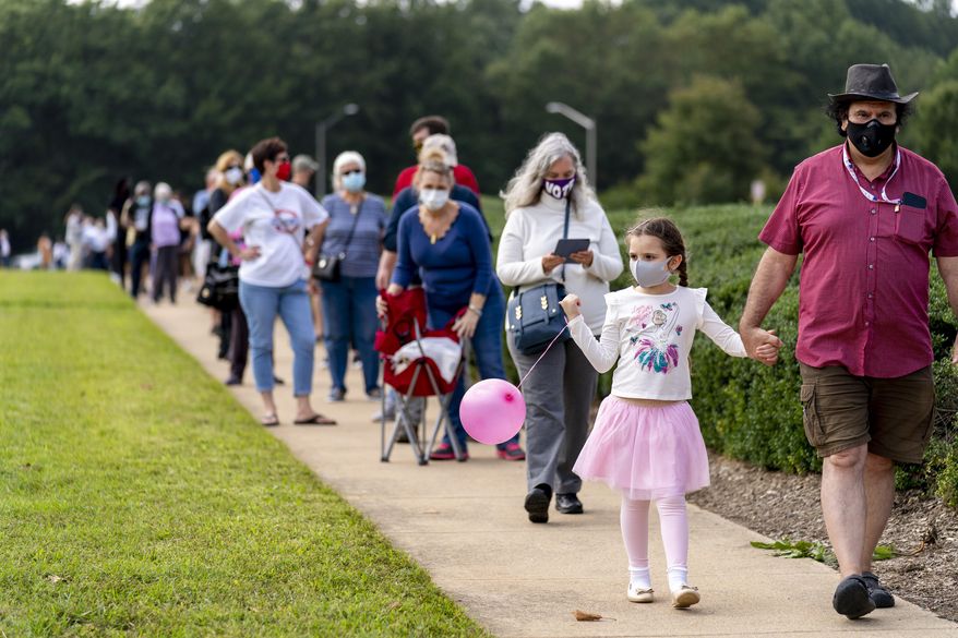 FILE- In this Sept. 18, 2020, file photo, Steven Daftarian of Fairfax, Va., and his daughter Laleh, 6, wait in a line stretching the equivalent of two football fields as hundreds line up for early voting at Fairfax County Government Center, in Fairfax, Va. Virginia voters this year will determine the staying power of a “blue wave” that flipped two competitive congressional districts two years ago, while also casting ballots for a U.S. Senate seat and the presidency. (AP Photo/Andrew Harnik, File)