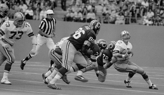 Dallas Cowboys&#39; quarterback Roger Staubach grimaces as he loses yards during second quarter action Nov. 28, 1974 in Irving, Texas. Making the tackle is Washington Redskins Verlon Biggs (86), Ron McDole (79) and Diron Talbert (72). (AP Photo/Ferd Kaufman)  **FILE**


