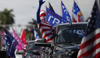 A man wearing a flag-themed body stocking waves from a car as hundreds of vehicles gather at Tropical Park ahead of a car caravan in support of President Donald Trump, in Miami, Sunday, Nov. 1, 2020.(AP Photo/Rebecca Blackwell)