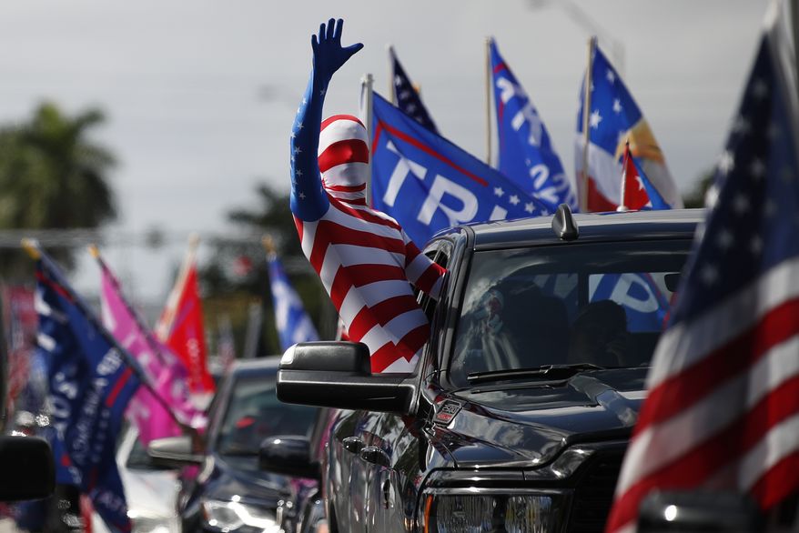 A man wearing a flag-themed body stocking waves from a car as hundreds of vehicles gather at Tropical Park ahead of a car caravan in support of President Donald Trump, in Miami, Sunday, Nov. 1, 2020.(AP Photo/Rebecca Blackwell)