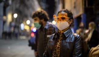 A woman wearing a face mask to help prevent the spread of coronavirus and a pair of glasses decorated for Halloween stands next to Sol square in Madrid, Spain, Saturday, Oct. 31, 2020. Nearly all Spaniards are facing a weekend with restrictions on leaving the regions where they live as authorities try to contain a sharp resurgence of reported coronavirus cases but refrain from a full lockdown to try to prevent further economic deterioration. (AP Photo/Manu Fernandez)