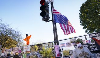 Pedestrians stand beside a fence covered in protest signs on the north side of the White House, Monday, Nov. 2, 2020, on a section of 16th Street renamed Black Lives Matter Plaza in Washington, on the day before the U.S. election. (AP Photo/John Minchillo)
