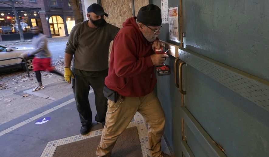 Ianni Stanciu, right, puts screws in a piece of lumber as he works to board up a Patagonia store in downtown Seattle, Monday, Nov. 2, 2020, the day before Election Day. Many businesses in the city boarded up windows Monday as a precaution against possible protests or violence on Election Day or the days following. (AP Photo/Ted S. Warren)