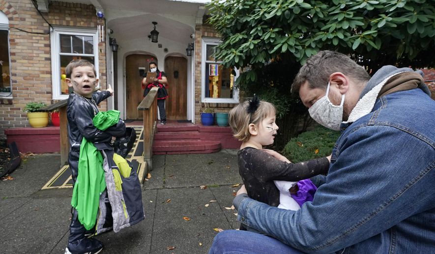 Alex Stonehill gets a goodbye from his daughter Helenore, 2, as her brother Malcolm, 4, motions to a friend arriving at the Community Day Center for Children on Thursday, Oct. 29, 2020, in Seattle. As more families make the jump back to group day care this fall in an attempt to restart lives and careers, many parents, pediatricians and care operators are finding that new, pandemic-driven rules offer a much-needed layer of safety but also seem incompatible with the germy reality of childhood. (AP Photo/Elaine Thompson)