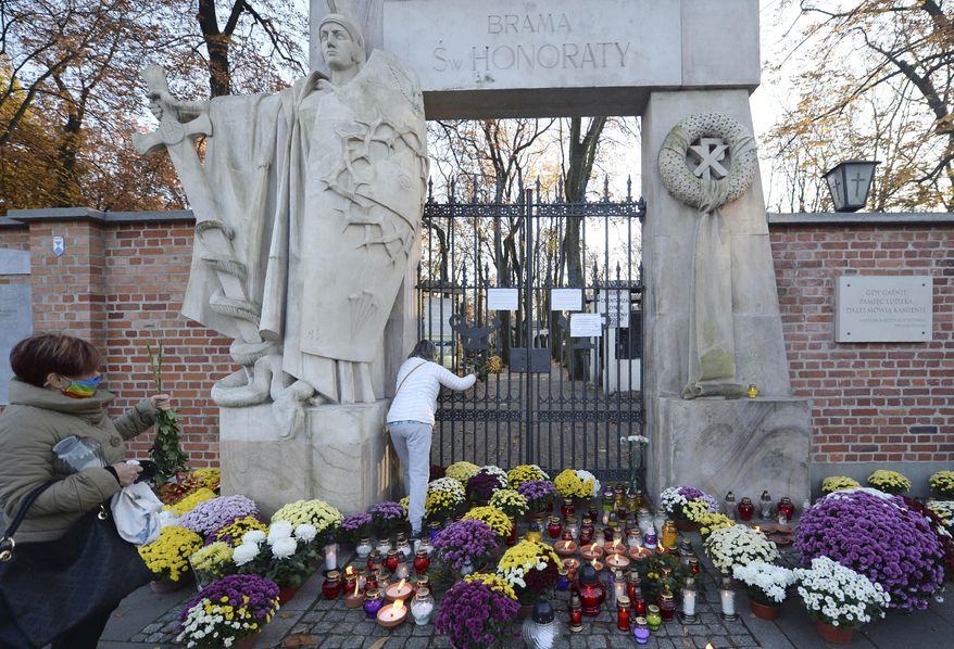 Flowers and candles people have placed outside of Powazki cemetery after Poland's government closed all cemeteries in an attempt to curb the spread of COVID-19, in Warsaw, Poland, Sunday, Nov. 1, 2020. Driven by new solidarity, Poles have been buying armloads of chrysanthemums to help out flower vendors who unexpectedly faced bankruptcy when the government ordered all cemeteries locked due to COVID-19 during a traditional memorial weekend. (AP Photo/Czarek Sokolowski)