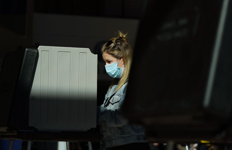 FILE - In this Friday, Oct. 30, 2020 file photo, a voter wears a face mask while casting her ballot in the atrium of Ball Arena, the home of the NBA's Denver Nuggets and the NHL's Colorado Avalanche, in Denver. (AP Photo/David Zalubowski, File)