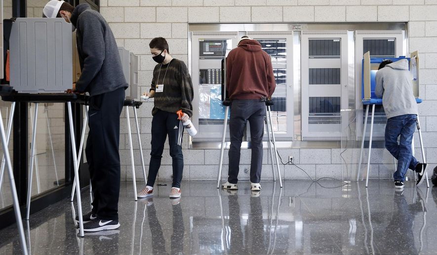 Emerson Dignan, a University of Iowa senior and first-time elections volunteer, sanitizes voting booths between voters during the 2020 Presidential election at the University of Iowa Campus Recreation and Wellness Center in Iowa City on Tuesday, Nov. 3, 2020. (Liz Martin/The Gazette via AP)