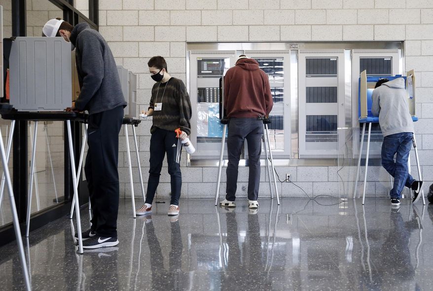 Emerson Dignan, a University of Iowa senior and first-time elections volunteer, sanitizes voting booths between voters during the 2020 Presidential election at the University of Iowa Campus Recreation and Wellness Center in Iowa City on Tuesday, Nov. 3, 2020. (Liz Martin/The Gazette via AP)