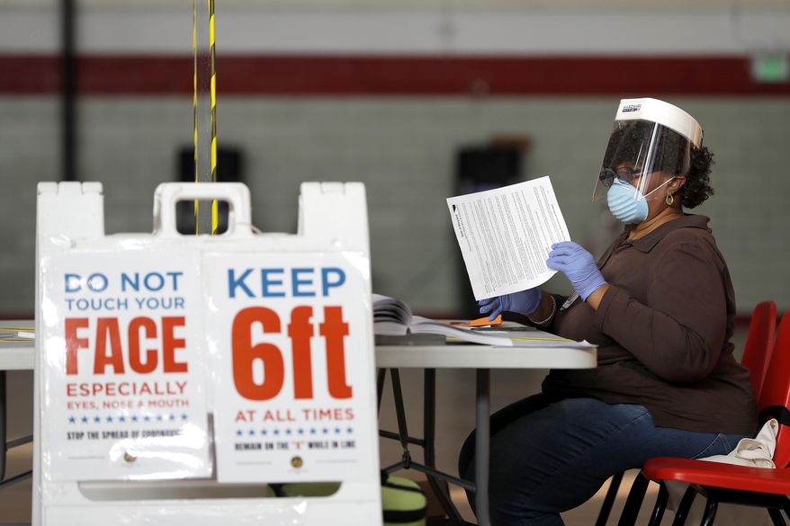 FILE - In this Tuesday, April 28, 2020, file photo, Louisa Boyer, a provisional election judge, reviews paperwork at a voting center at Edmondson High School as voters arrive to cast their ballot in the 7th Congressional District special election in Baltimore. Many Maryland voters have already mailed in their ballots amid the coronavirus pandemic, or voted early. Those who waited for Election Day will be voicing their choices on Tuesday for president and the state's eight members of the U.S. House of Representatives. (AP Photo/Julio Cortez, File)